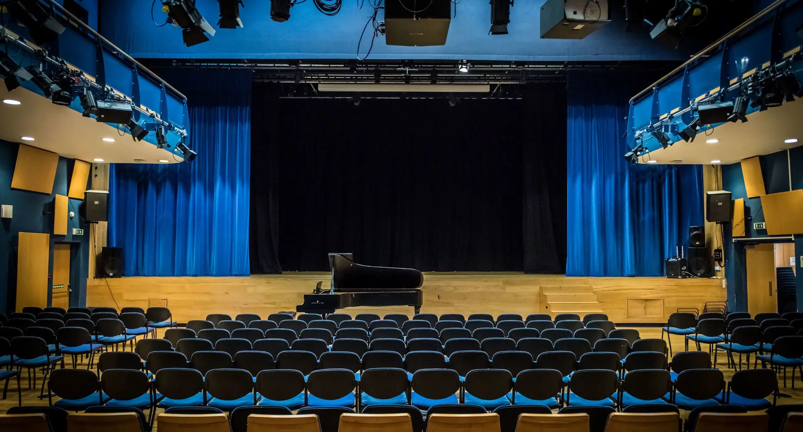 Harvey Hall, an assembly hall where rows of blue chairs face a black piano atop a stage